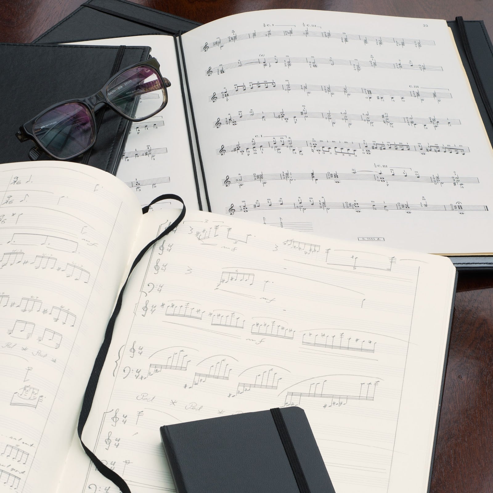 Music sheets with a notebook and glasses on a wooden surface