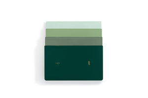A stack of four slim rectangular notebooks or journals in shades of green, with the top two in pale green and the bottom two in darker green, including a dark forest green cover with gold foil text and logo, set against a plain white background.
