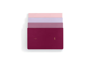 Four slim rectangular notebooks or journals stacked vertically on a white background, with the top three fanned out slightly. The bottom notebook is a deep burgundy/magenta color with a small gold logo, while the others show pink, lavender, and mauve tones.
