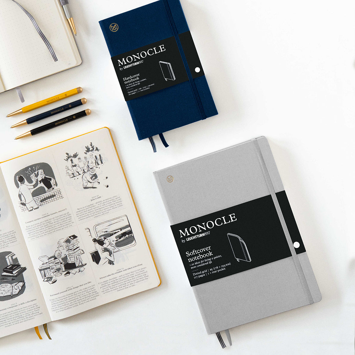 Two notebooks, one open with illustrations, the other closed, on a white surface with stationery items.