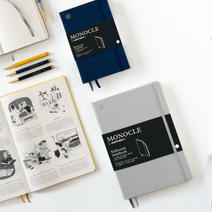 Two notebooks, one open with illustrations, the other closed, on a white surface with stationery items.