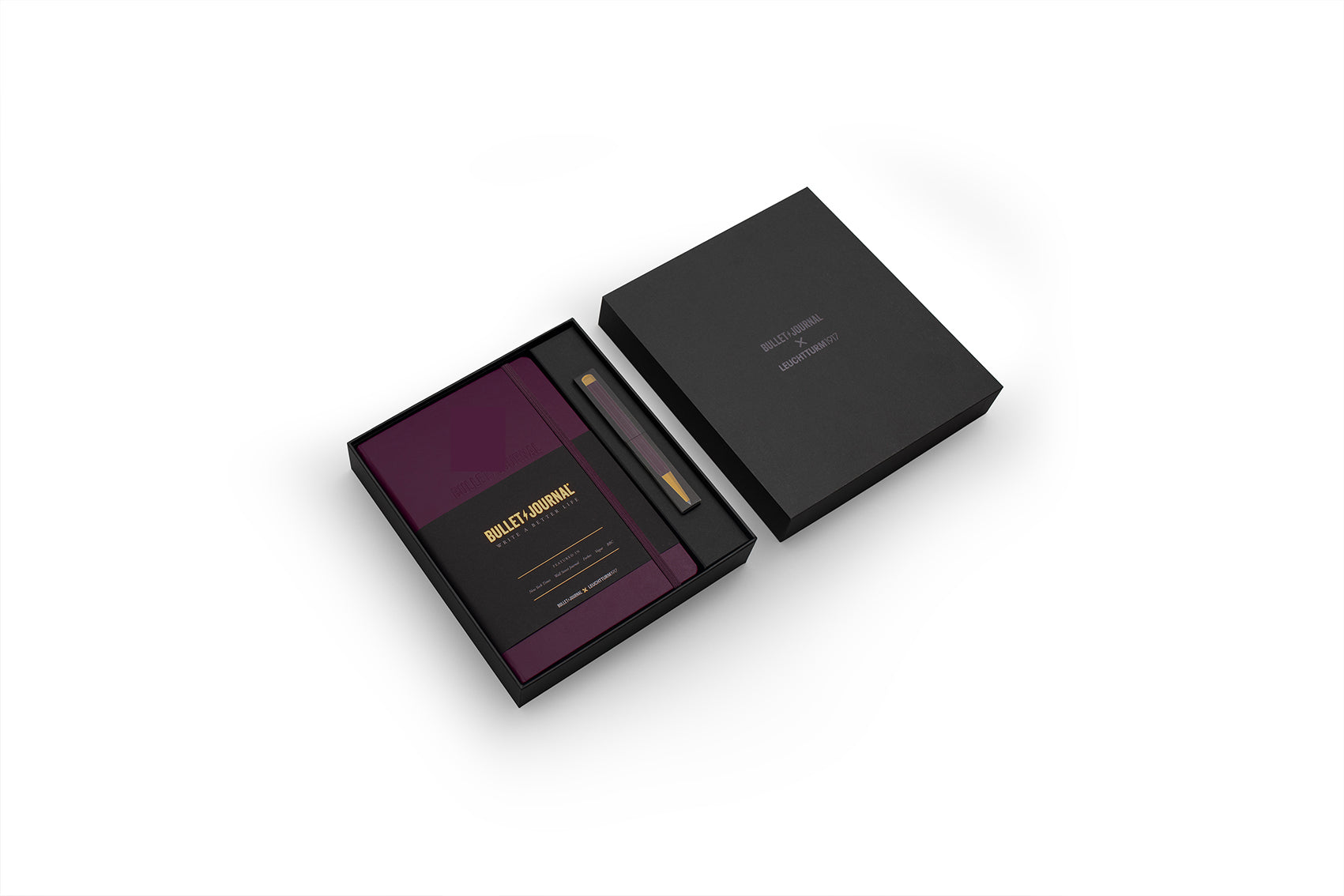 A luxury gift set featuring a black rectangular box with its lid placed beside it, containing a deep purple notebook or booklet with gold lettering and a slim black pen with gold accents.