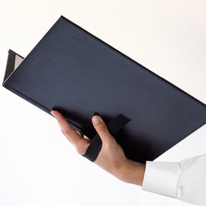 Hand holding a black leather-bound book on a white background