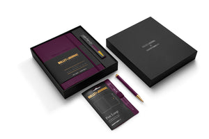A premium gift set from Bullet Journal Club, featuring a black notebook with a deep purple cover, a matching purple and gold pen, a black branded box, a card, and a pen loop, arranged on a clean white background.