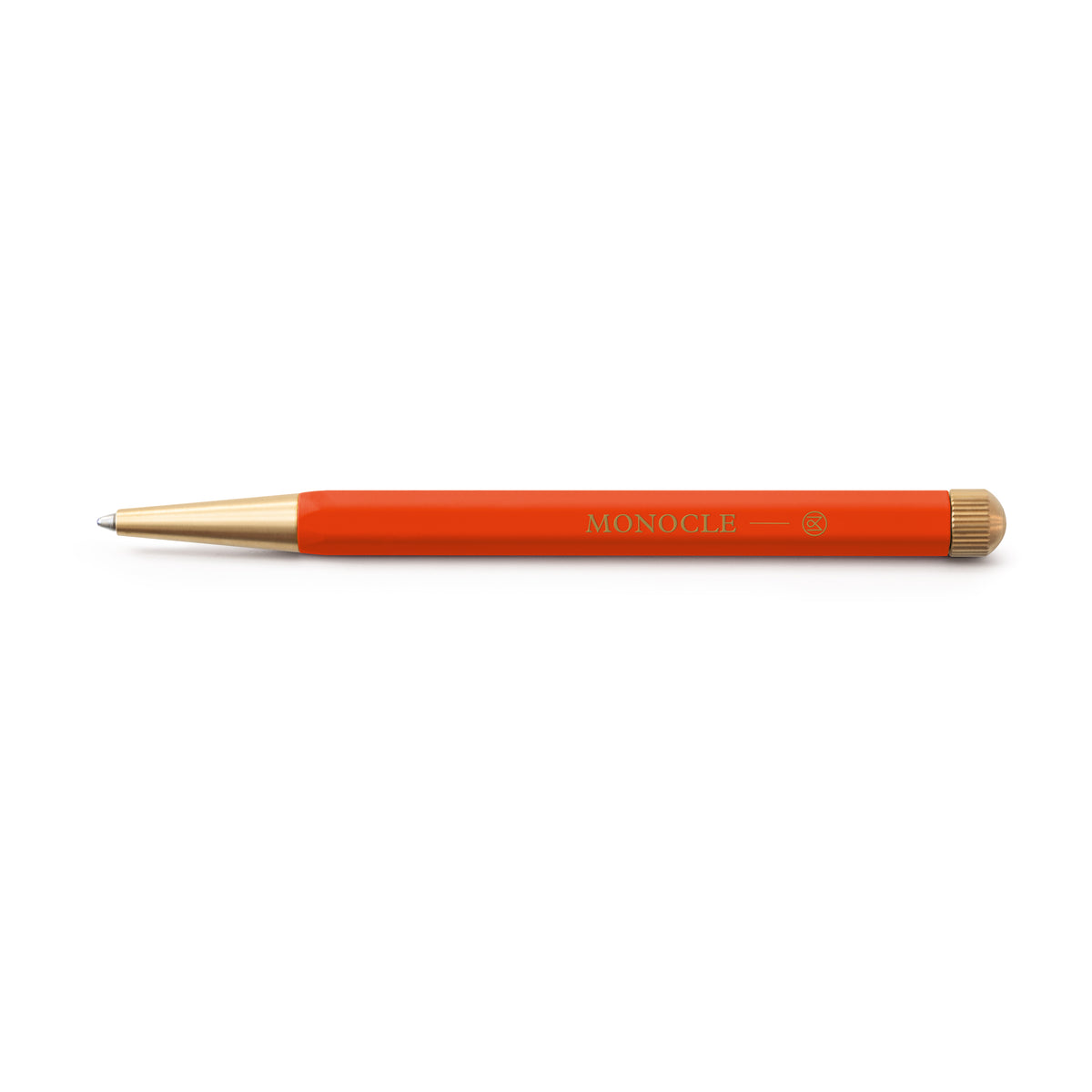 An orange-red ballpoint pen with gold accents, featuring the brand name 'MONOCLE' printed in gold on the barrel, set against a plain white background.