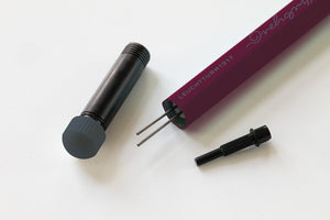 A Leuchtturm1917 electric arc light tube kit shown disassembled on a clean white background, featuring a dark purple cylindrical body with white text, a black metal canister, and two black terminal connectors.