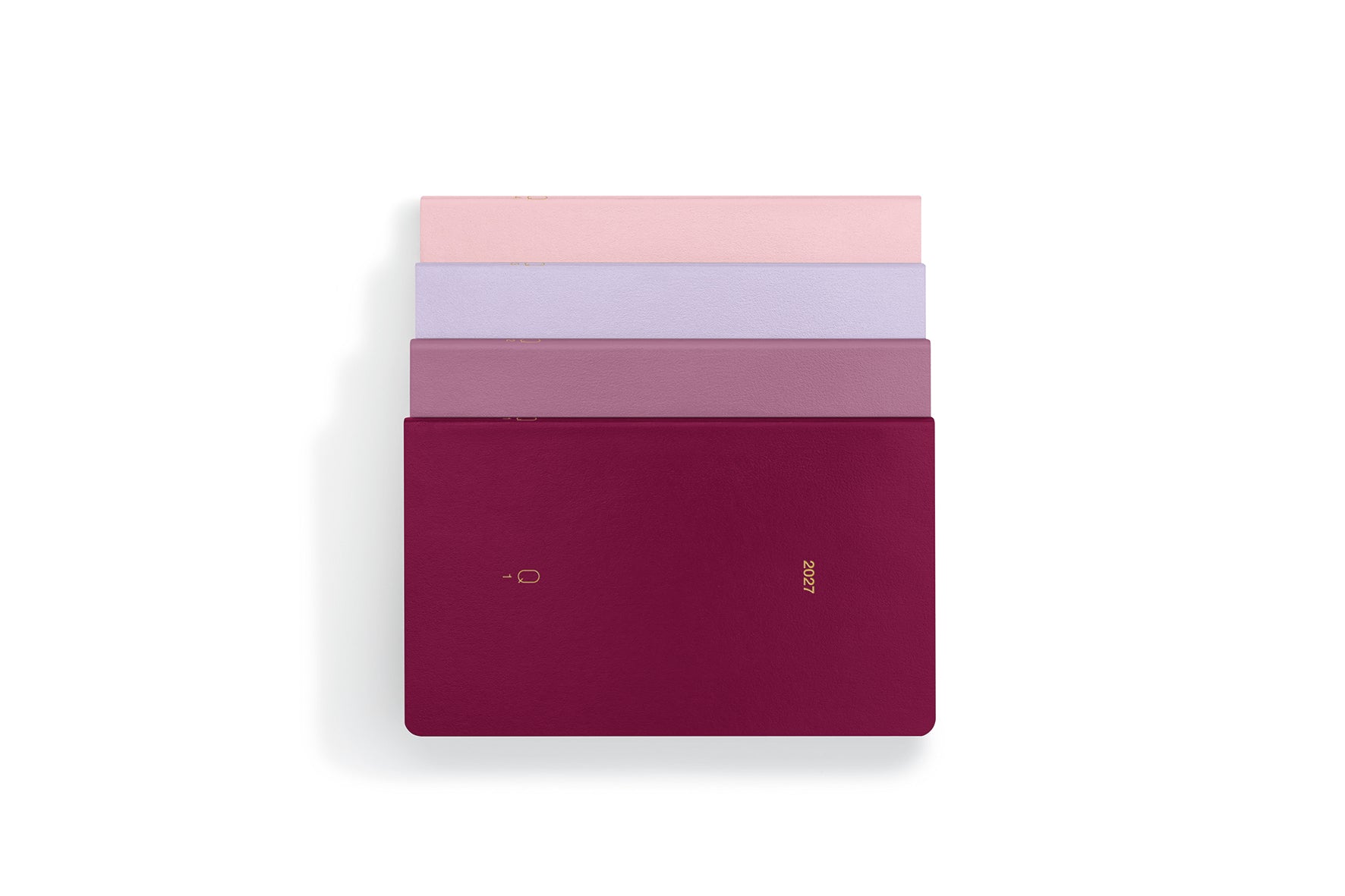 Four slim rectangular notebooks or journals stacked vertically on a white background, with the top three fanned out slightly. The bottom notebook is a deep burgundy/magenta color with a small gold logo, while the others show pink, lavender, and mauve tones.