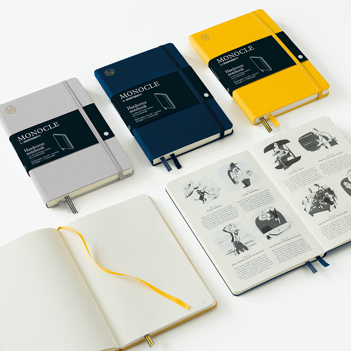 Three closed Monocle notebooks in gray, navy blue, and yellow are arranged on a white surface, alongside two open notebooks showing printed pages and ribbon bookmarks.